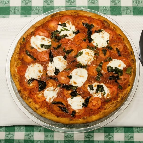 A Pizza Spot Margherita pizza with fresh tomatoes, mozzarella, and basil on a checkered tablecloth.
