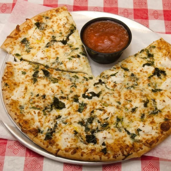 White pizza with spinach and ricotta cheese, served with a side of marinara sauce on a checkered tablecloth.