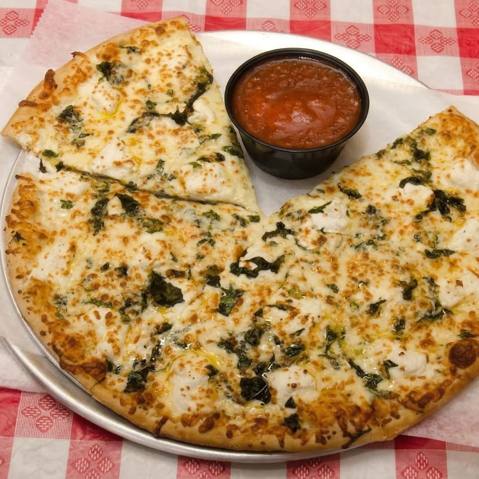 White pizza with spinach and ricotta cheese, served with a side of marinara sauce on a checkered tablecloth.