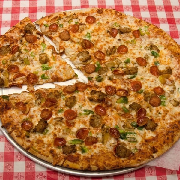 A large Pizza Spot pizza with pepperoni, sausage, and green peppers on a red and white checkered tablecloth.