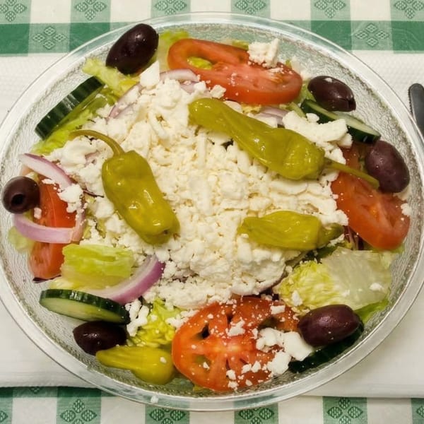 A vibrant Greek salad with lettuce, tomatoes, cucumbers, olives, feta, and pepperoncini.