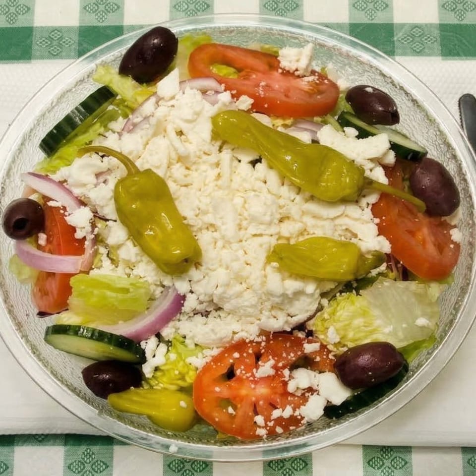 A vibrant Greek salad with lettuce, tomatoes, cucumbers, olives, feta, and pepperoncini.