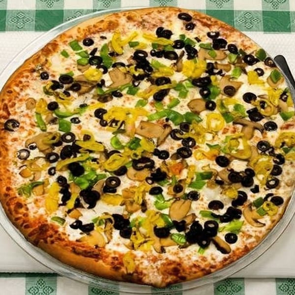 A Pizza Spot pizza with black olives, green peppers, mushrooms, and banana peppers on a checkered tablecloth.