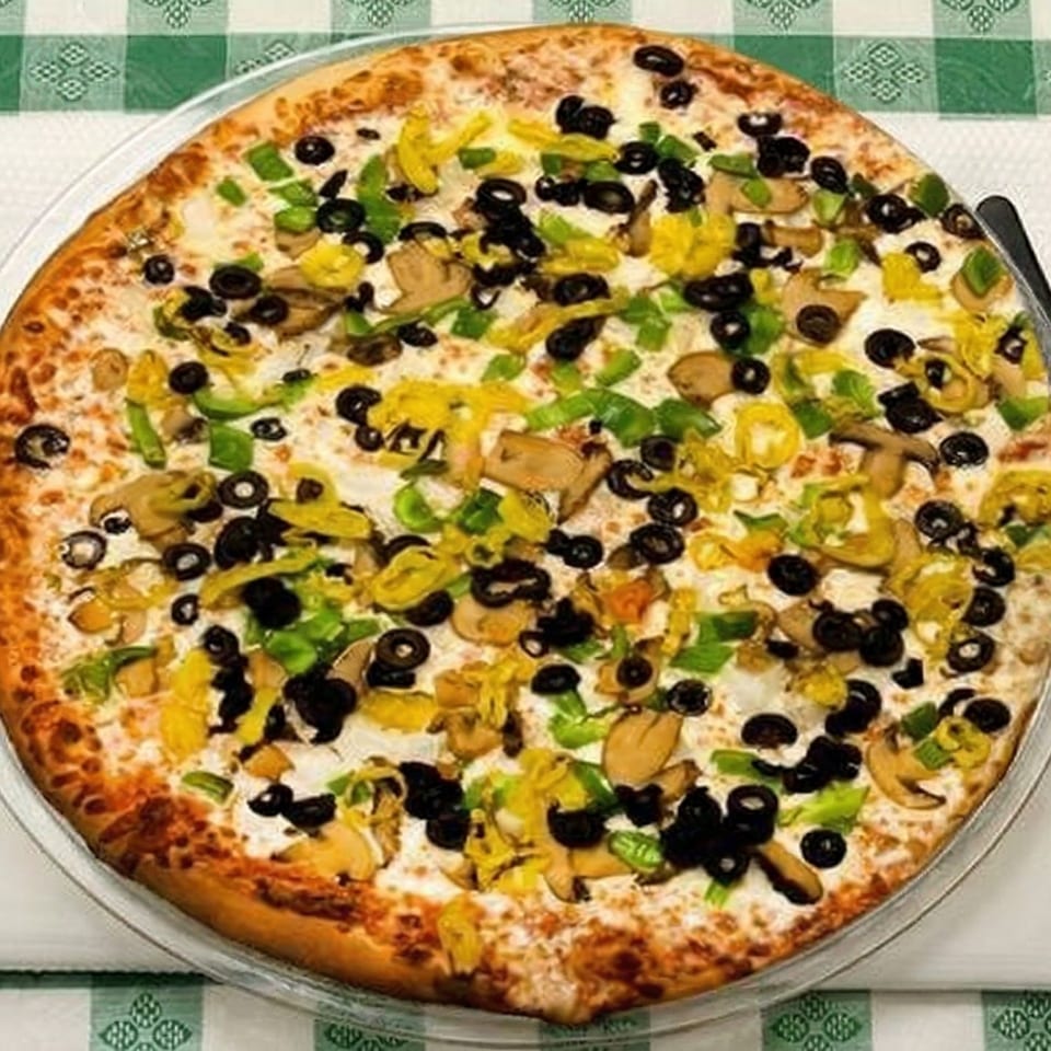 A Pizza Spot pizza with black olives, green peppers, mushrooms, and banana peppers on a checkered tablecloth.